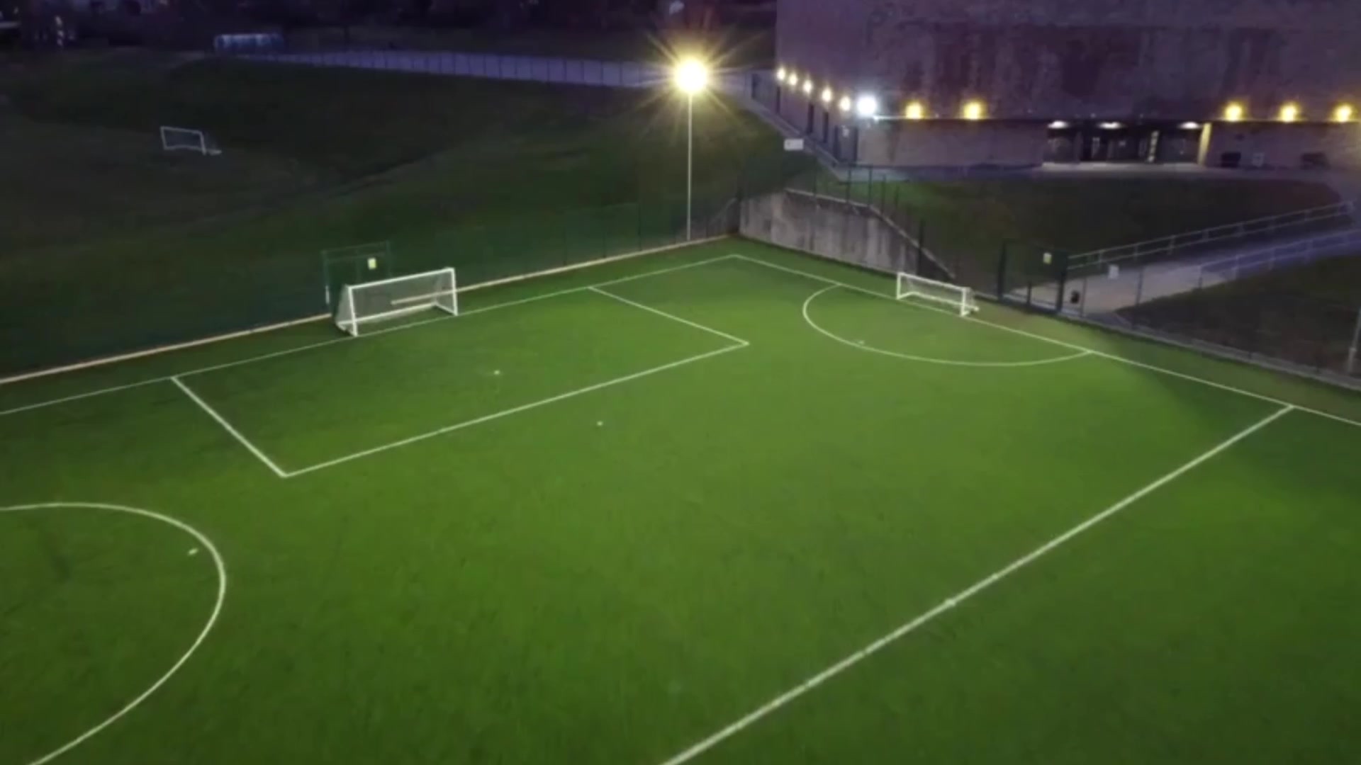 A floodlit artificial football pitch seen from above at dusk